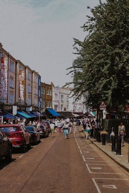 The image depicts a row of light blue and beige multi-story residential buildings with classic architectural details, including bay windows and decorative trim, set along a street in Notting Hill. The