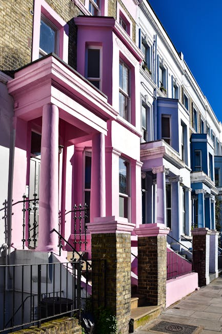 A row of multi-story residential buildings in Notting Hill with a variety of pastel-colored facades including shades of blue, pink, and white. The buildings feature large sash windows, some with flower pots on window sills and small front gardens with wrought iron fences. The surfaces include brickwork and painted exteriors, appearing clean and well-maintained under natural daylight, highlighting the intricate architectural details. This image reflects outdoor residential architecture, with no cleaning tools or surfaces visible, emphasizing the vibrant street aesthetic associated with the area. Carpet Cleaning Notting Hill specializes in surface cleaning and deep cleaning services to maintain the hygiene and appearance of similar residential exteriors.